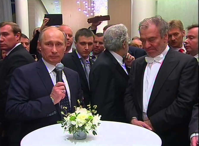 O presidente russo Vladimir Putin e o maestro Valery Gergiev em anúncio de investimento na sala de concertos de São Petersburgo; entre eles, de costas, o tenor Placido Domingo [Reprodução/YouTube]